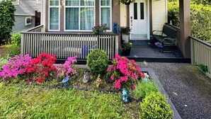 A two-story house with a covered porch and a front yard with colorful flowers. - Private Studio: Separate Entry, Washroom & Living Room (Surrey)