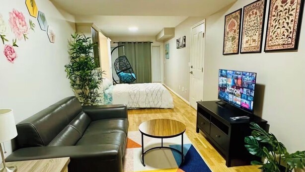 A modern living room with a sofa, a coffee table, a TV, and a bed in the background. - Private Studio: Separate Entry, Washroom & Living Room (Surrey)