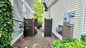 A narrow brick pathway flanked by two houses with white siding and dark shutters, leading to a gated entrance. - Private Studio: Separate Entry, Washroom & Living Room (Surrey)