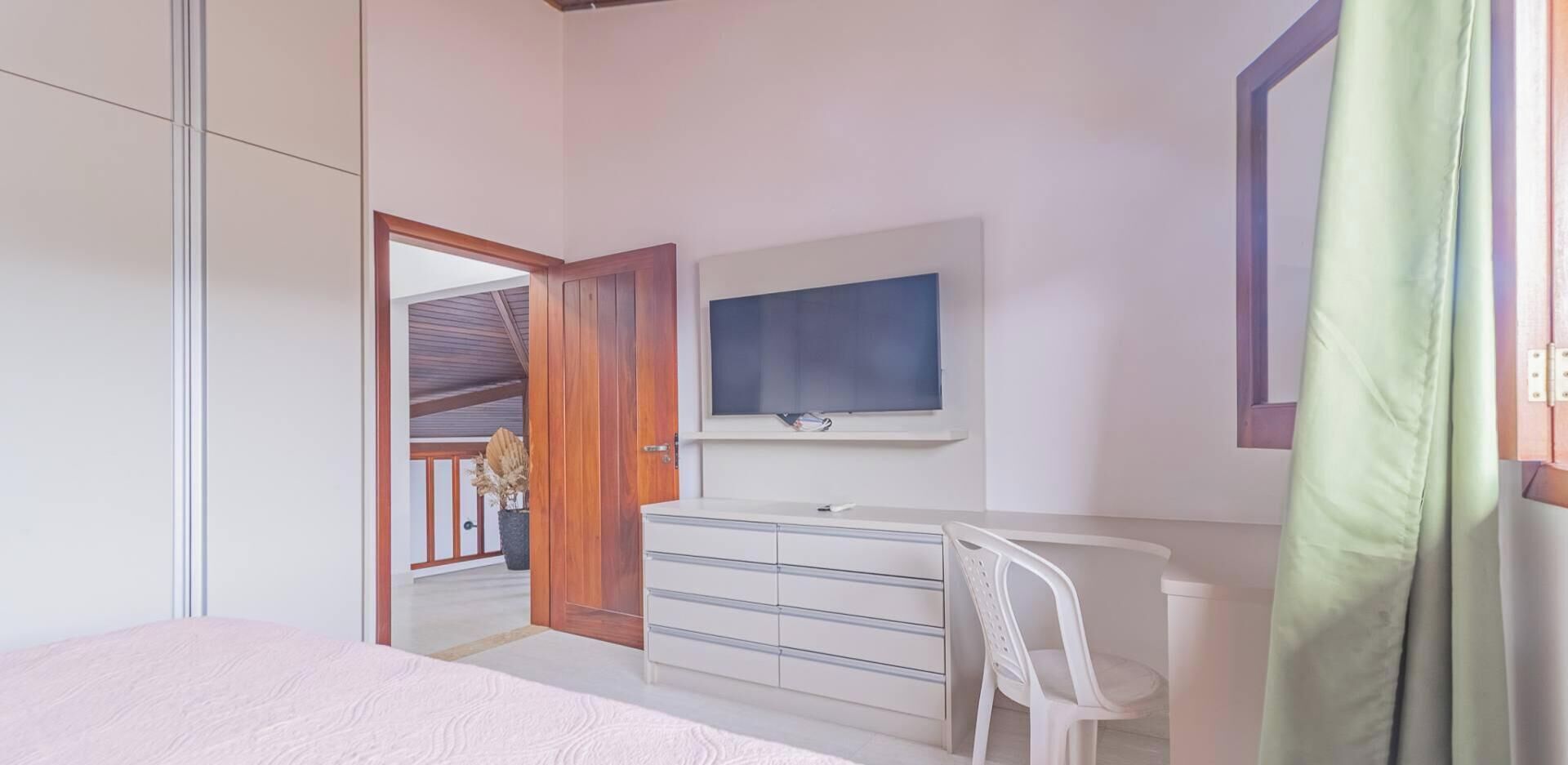 Une chambre à coucher avec un lit, une commode, un téléviseur et une fenêtre avec un rideau.