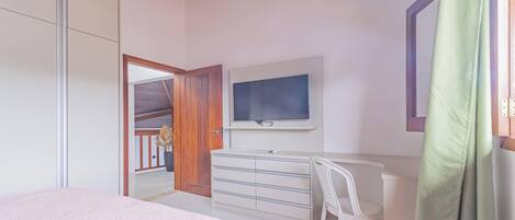 Une chambre à coucher avec un lit, une commode, un téléviseur et une fenêtre avec un rideau.
