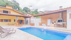 A swimming pool with lounge chairs, a barbecue area, and a covered patio. - Casa em Ubatuba com churrasqueira e varanda ampla (Ubatuba)