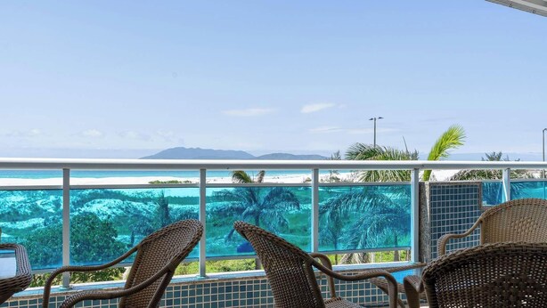 A balcony with wicker chairs overlooking a pool and a beach. - Apto em Cabo Frio em Frente a Praia com Varanda (Cabo Frio)
