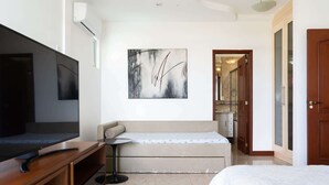 A modern hotel room with a flat-screen TV, a sofa, a small table, and a painting on the wall. - Apto em Cabo Frio em Frente a Praia com Varanda (Cabo Frio)