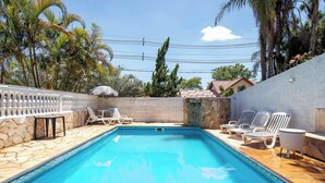 A swimming pool with lounge chairs and a stone wall. - Sitio em Aracariguama com Piscina e Churrasqueira (Araçariguama)