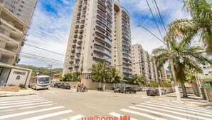 Un immeuble résidentiel à plusieurs étages, doté de balcons, d’un passage pour piétons et de palmiers.