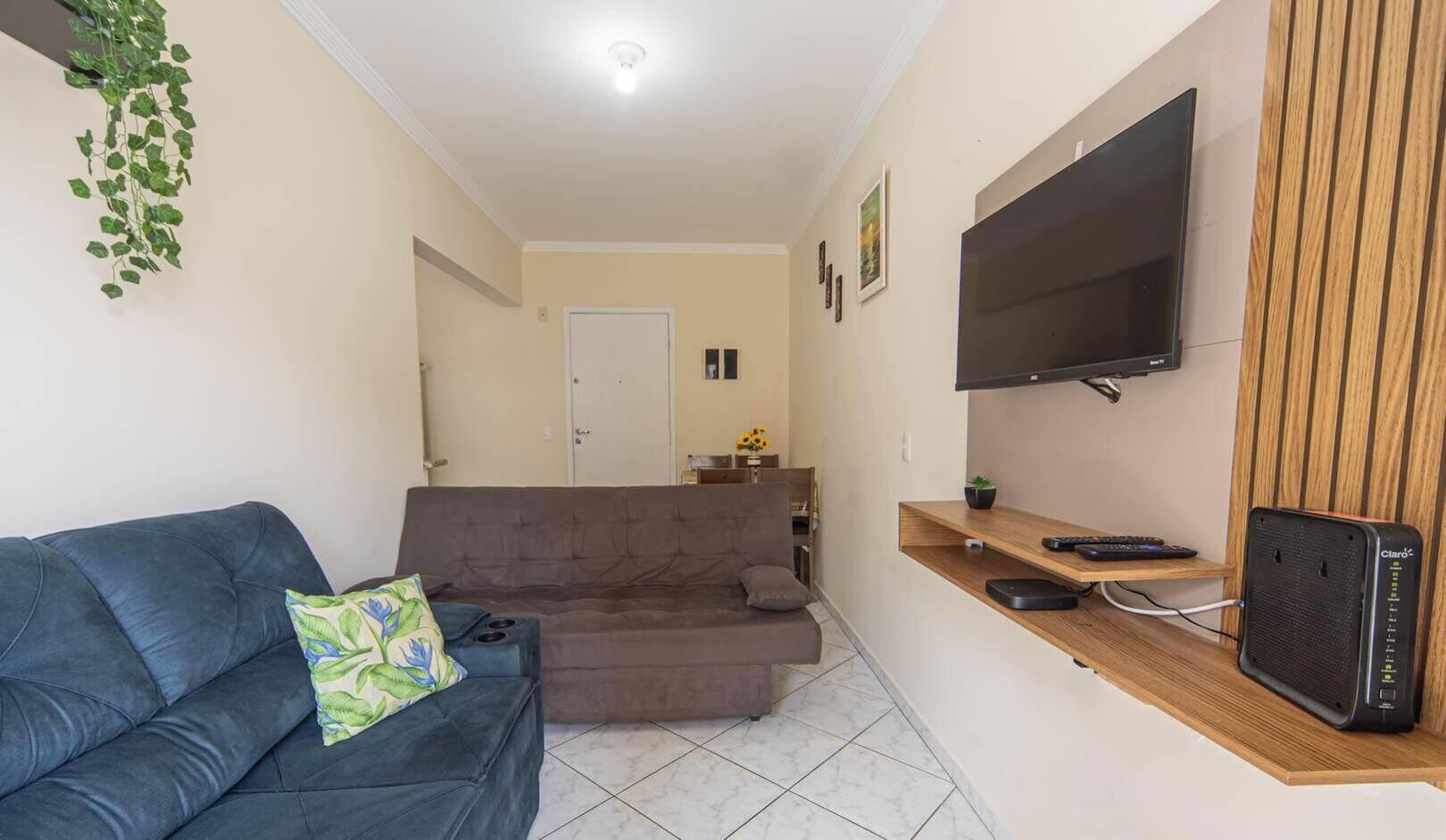 A living room with a blue sofa, a brown sofa, a TV mounted on a wooden shelf, and a speaker.