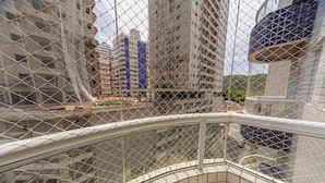 Une vue à travers une clôture en treillis métallique d’un bâtiment en construction, doté de plusieurs étages et d’une bande verticale bleue.