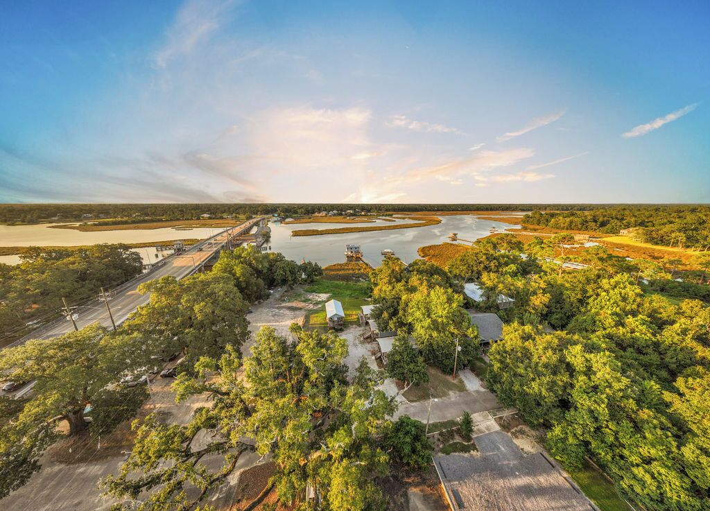 An aerial view of a residential area with a river, a bridge, and scattered houses surrounded by greenery.