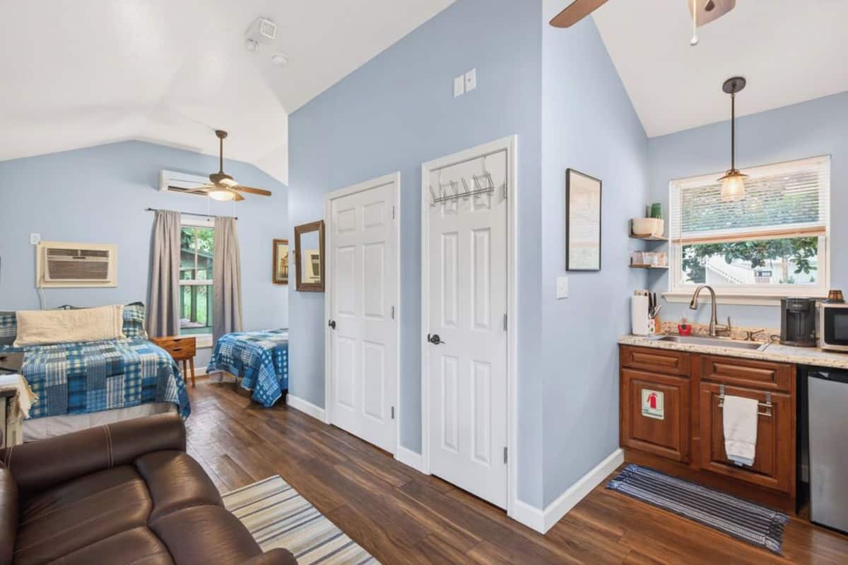 A well-lit room with a bed, a sofa, a desk, and a kitchenette.