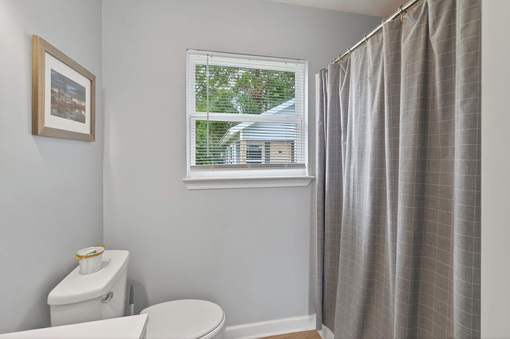 A bathroom with a toilet, a window with blinds, and a shower curtain.