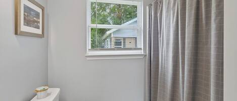A bathroom with a toilet, a window with blinds, and a shower curtain.