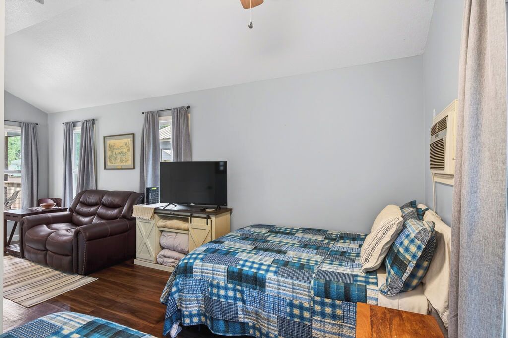 A bedroom with a bed, a reclining chair, a desk with a television, and a window with curtains.