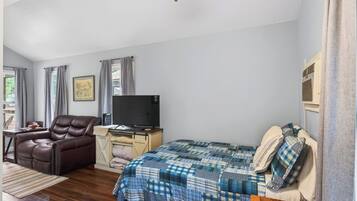 A bedroom with a bed, a reclining chair, a desk with a television, and a window with curtains.