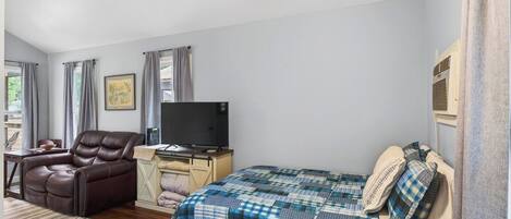 A bedroom with a bed, a reclining chair, a desk with a television, and a window with curtains.