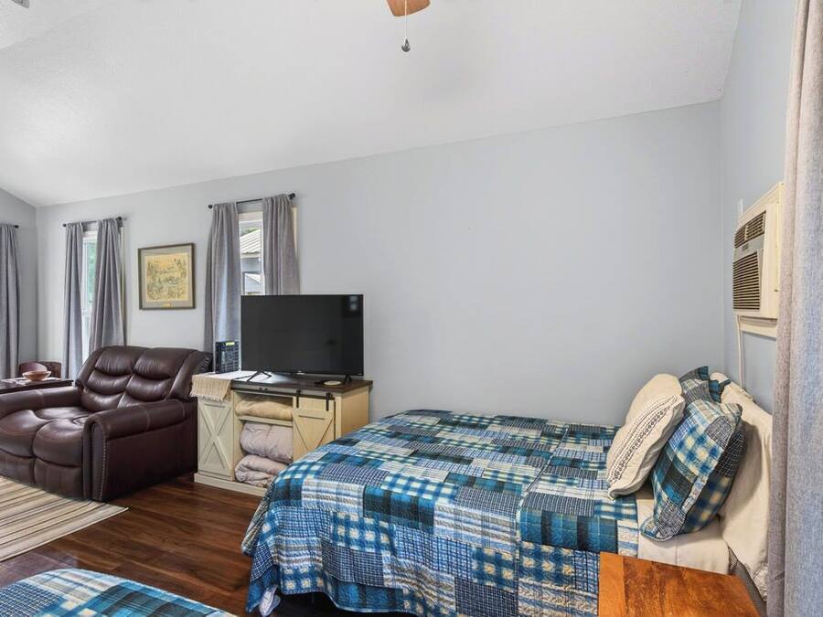 A bedroom with a bed, a reclining chair, a desk with a television, and a window with curtains.