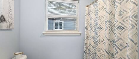 Un baño con inodoro, ventana y cortina de ducha.