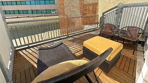 An outdoor seating area with wicker furniture and a yellow cushion, a glass balustrade, and a brick wall.