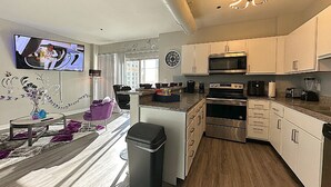 A modern kitchen with stainless steel appliances, a dining area with a purple chair, and a TV mounted on the wall.
