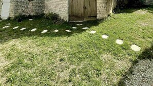 A stone building with a wooden door, surrounded by grass and a clear sky. - Le Nid Charentais (Rouillac)