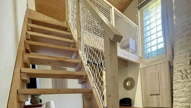 A wooden staircase with a mesh railing leading to a loft area. - Le Nid Charentais (Rouillac)