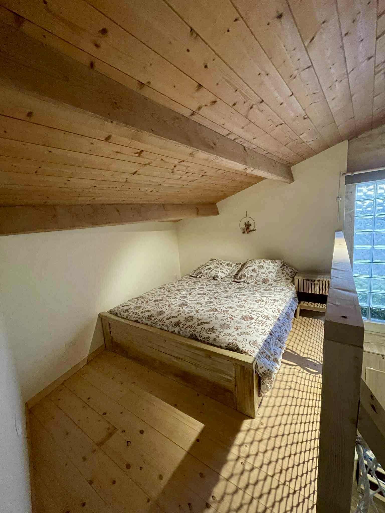 A bedroom with a wooden ceiling, a bed with floral bedding, and a window with a view.