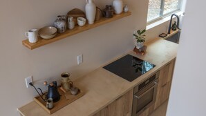 A kitchen with a wooden countertop, a black induction cooktop, a stainless steel oven, and a wooden shelf above holding various ceramic and glassware. - Highland Cows/Wood-Fired Hot Tub/Stunning Views (Logan)