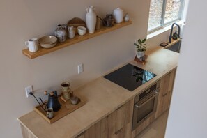 A kitchen with a wooden countertop, a black induction cooktop, a stainless steel oven, and a wooden shelf above holding various ceramic and glassware. - Highland Cows/Wood-Fired Hot Tub/Stunning Views (Logan)