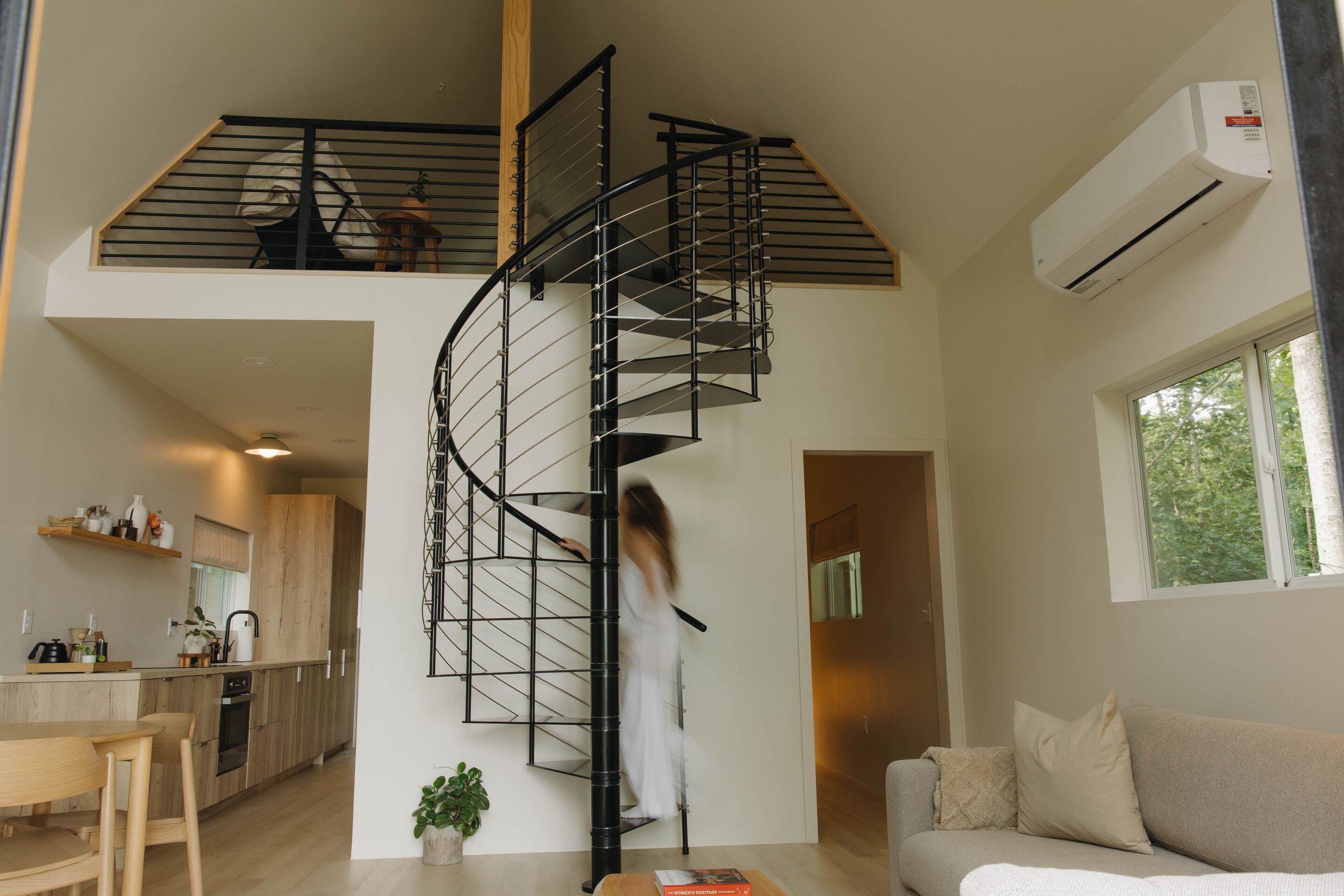 A modern interior with a spiral staircase, a kitchen, a living area, and a window with a view.