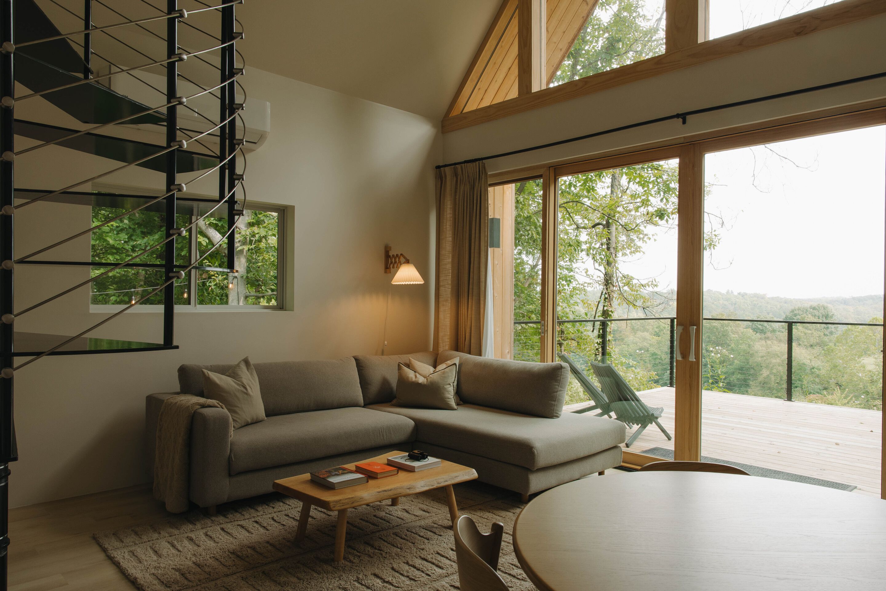 A modern living room with a sectional sofa, a coffee table, and a view of a balcony with a wooden railing.