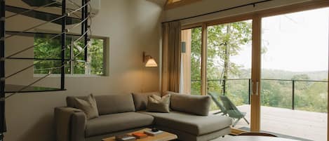A modern living room with a sectional sofa, a coffee table, and a view of a balcony with a wooden railing.