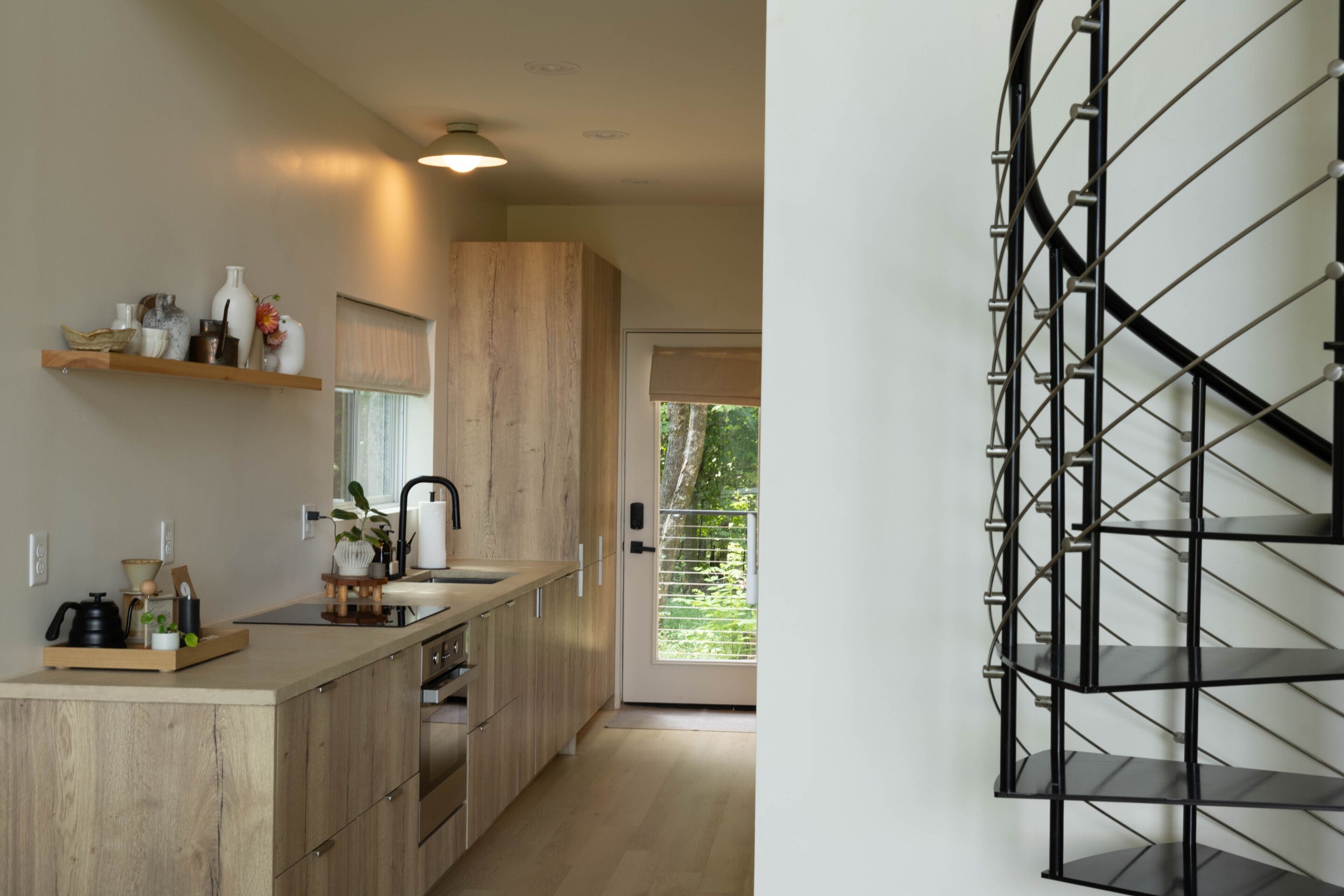 A modern kitchen with wooden cabinets, a black countertop, and a window with a view of greenery.