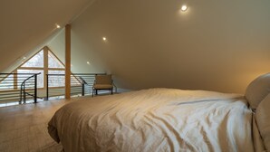 A bedroom with a large bed, a chair, and a skylight. - Highland Cows/Wood-Fired Hot Tub/Stunning Views (Logan)