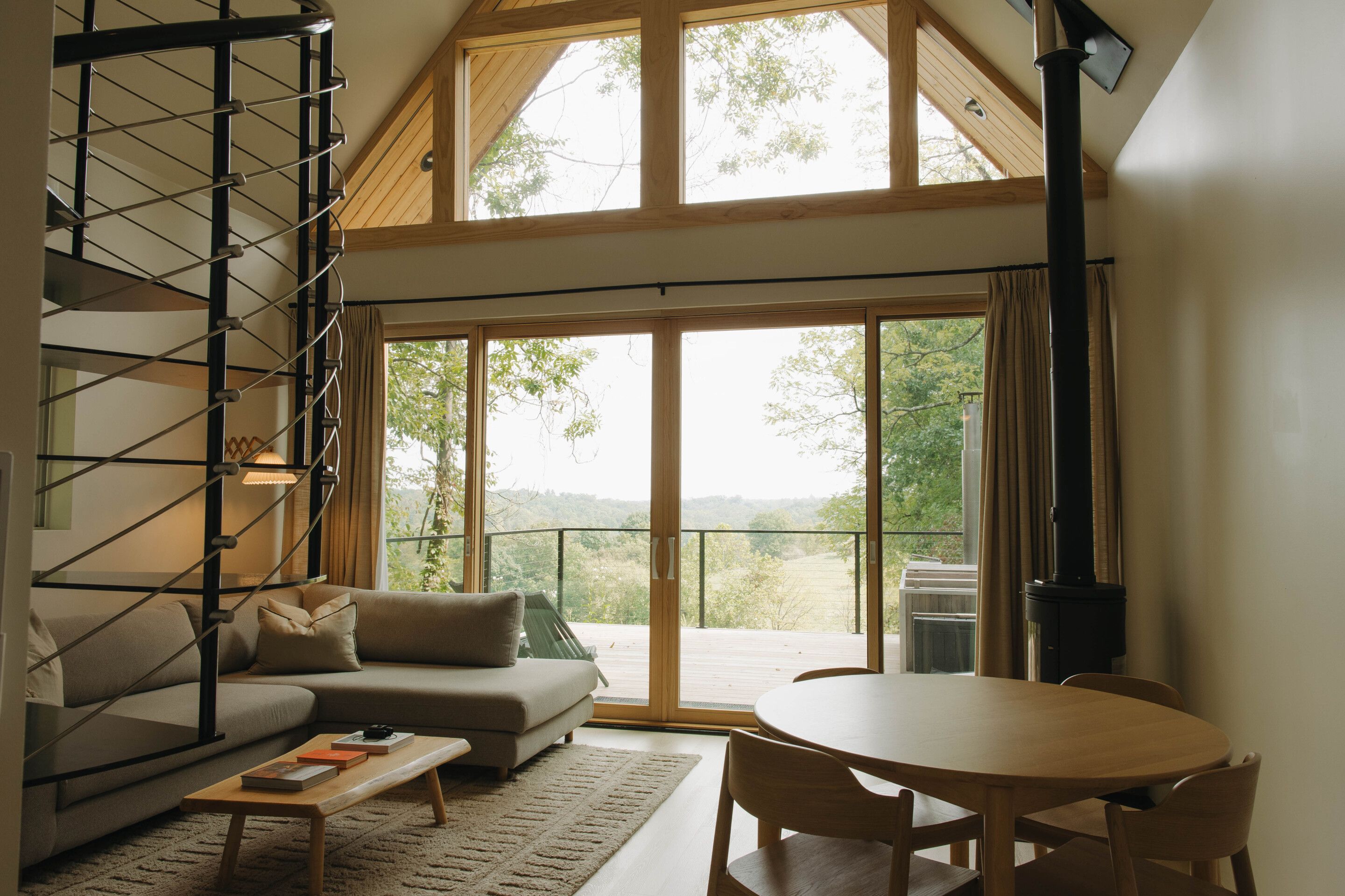 A spacious living area with a sofa, a coffee table, and a dining table. There is a large window providing a view of the outdoors.
