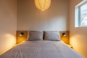 A neatly made bed with a headboard, two bedside lamps, and a window with a view of trees. - Highland Cows/Wood-Fired Hot Tub/Forest Escape (Logan)