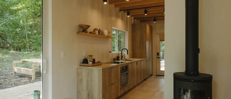 A modern kitchen with wooden cabinetry, a central island, and a wood-burning stove.