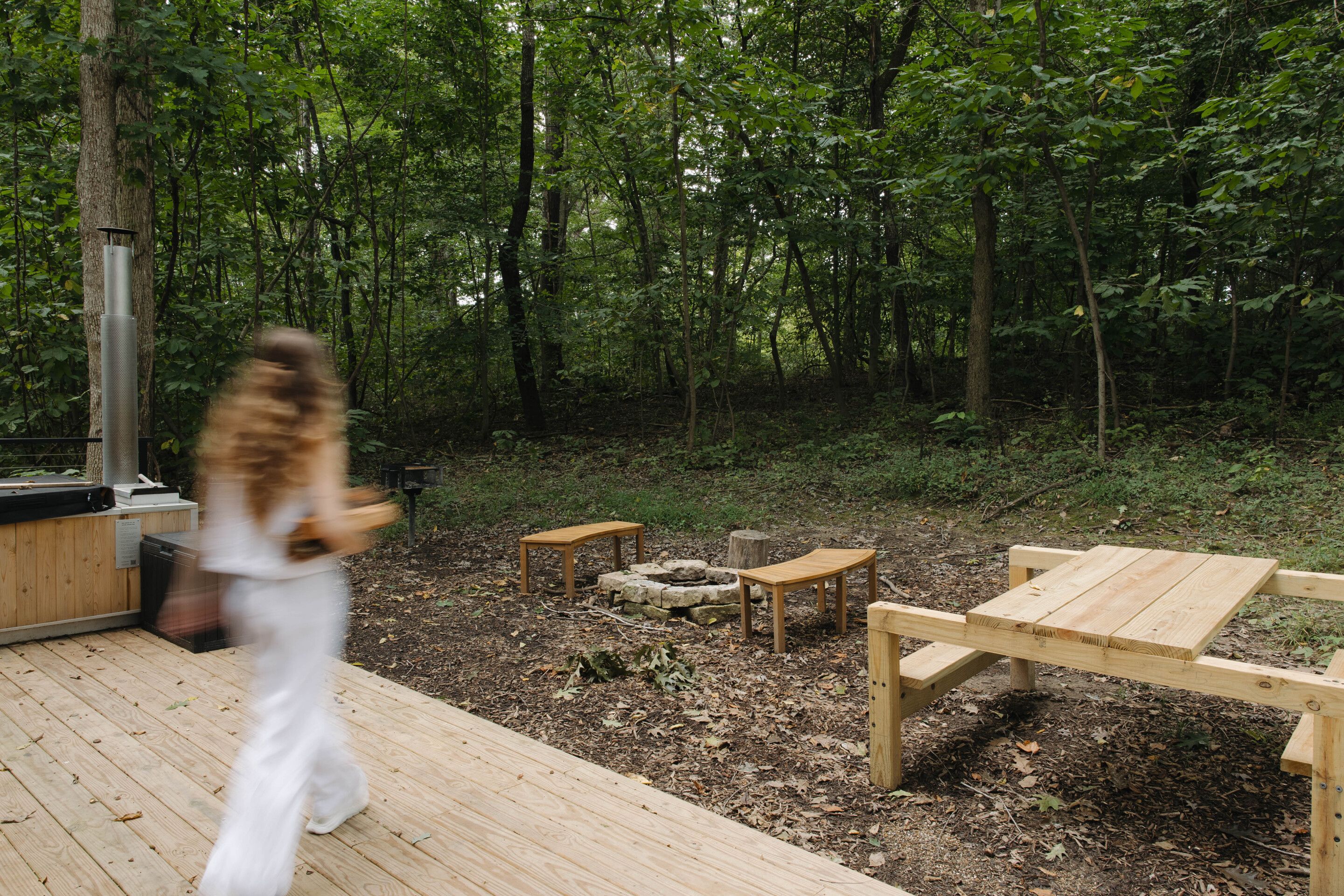 A wooden deck with a table and benches, surrounded by a forested area.