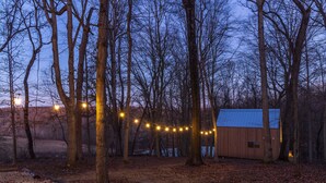 Une cabane en bois entourée d’arbres, illuminée de guirlandes lumineuses.