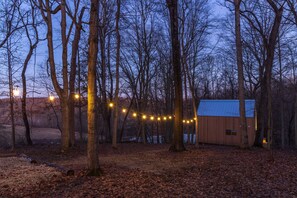 A wooden cabin surrounded by trees with string lights. - Highland Cows/Wood-Fired HotTub/Peaceful Pond View (Logan)