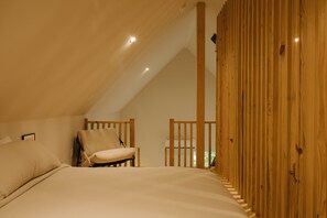 Une chambre avec un plafond en pente, un lit, une chaise et un lambris en bois sur un des murs.