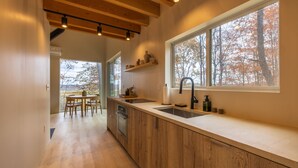 Une cuisine moderne avec des meubles en bois, une grande fenêtre et un coin repas comprenant une table et des chaises.