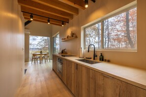 A modern kitchen with wooden cabinets, a large window, and a dining area with a table and chairs. - Highland Cows/Wood-Fired HotTub/Peaceful Pond View (Logan)