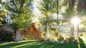 A rustic wooden cabin with a stone foundation, surrounded by lush greenery and a sign reading "Pack Creek Ranch."