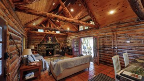 A log cabin interior with a fireplace, wooden furniture, and a stone wall.