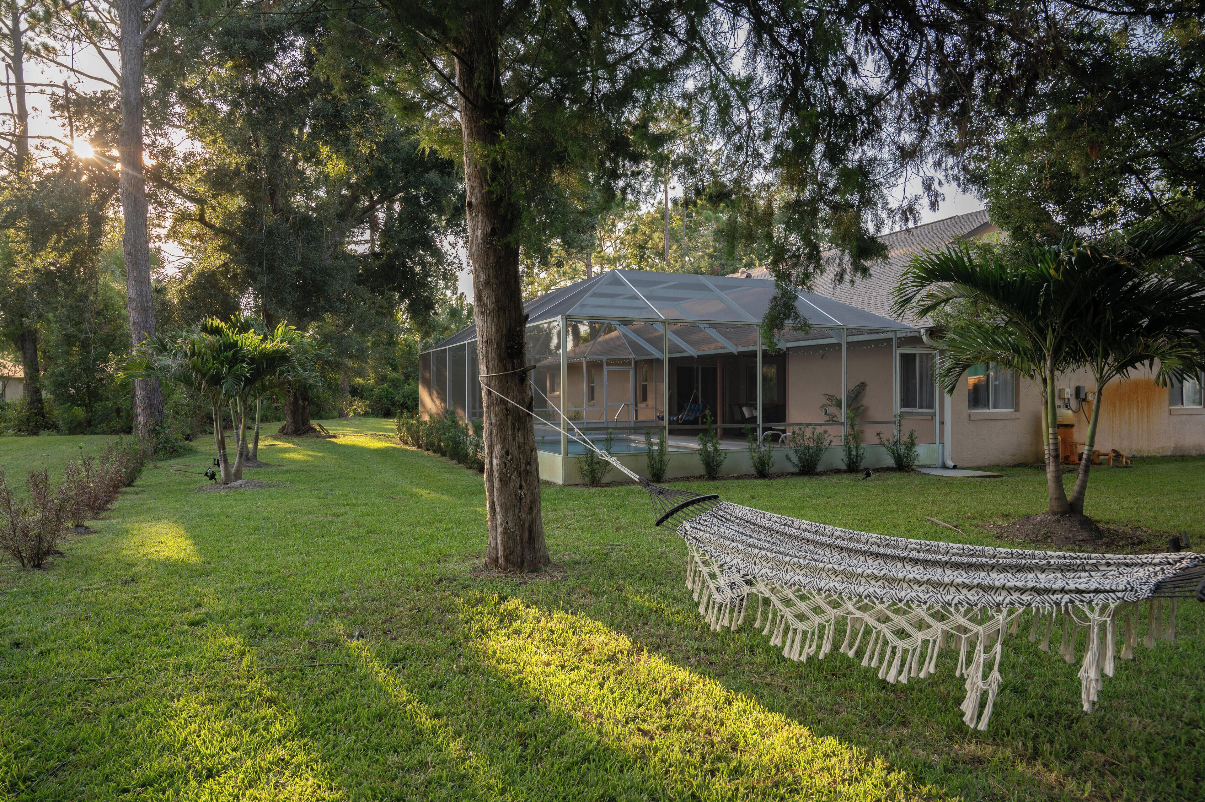 A house with a covered patio, surrounded by trees and a hammock.