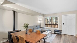 Een moderne woonkamer met een houten eettafel, twee banken, een salontafel en een groot raam met uitzicht op bomen.