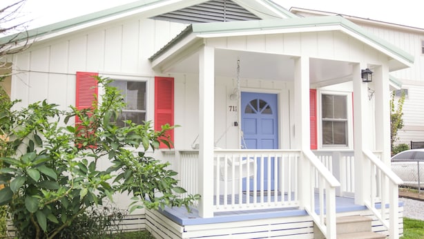 Una casa blanca con puerta azul, contraventanas rojas y un porche con escalones.