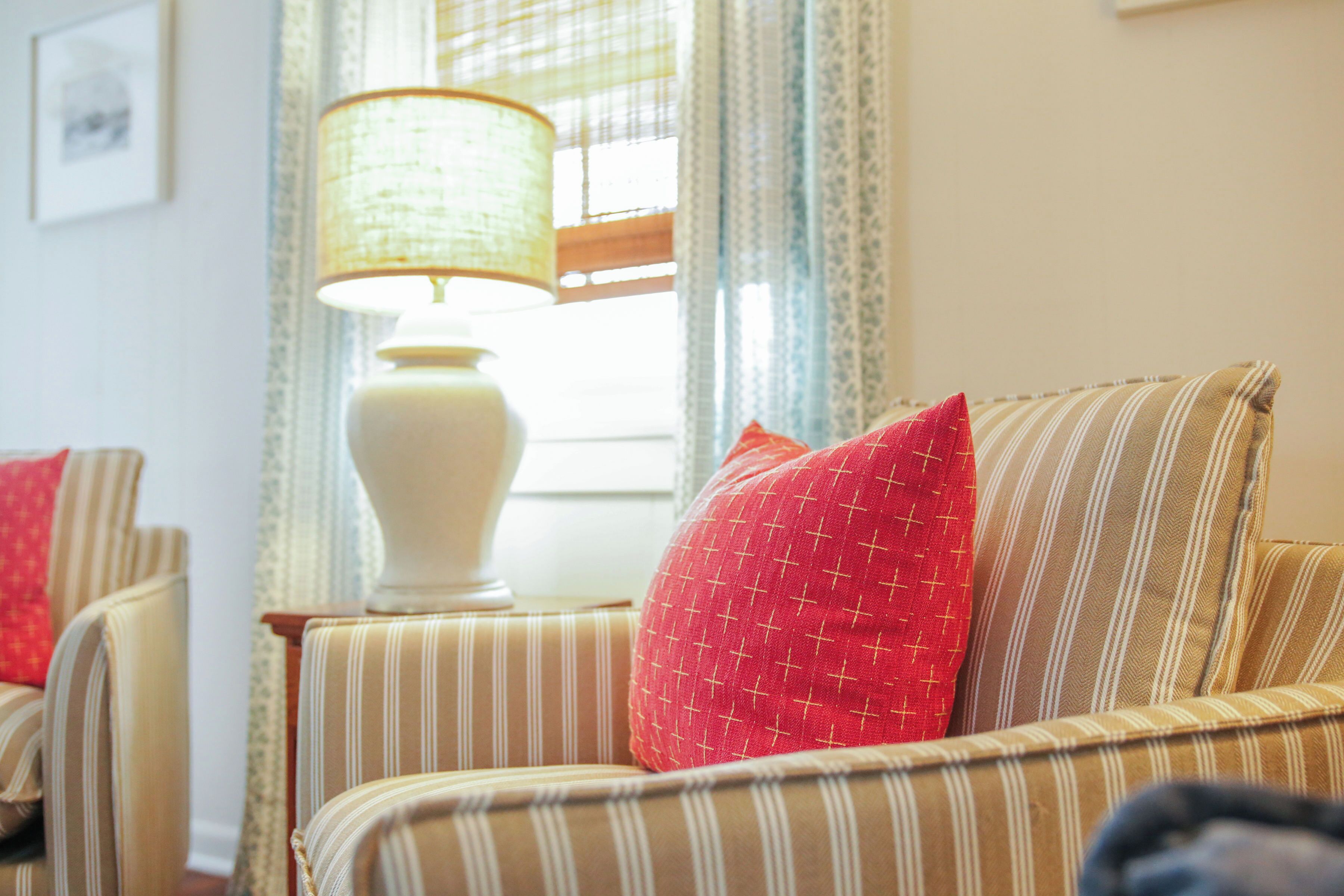 A striped armchair with a red pillow, a white lamp, and a window with curtains.
