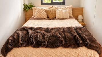 A bed with a quilted headboard, a fluffy brown throw blanket, and a bedside lamp.