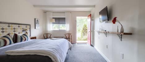 A bedroom with a bed, a TV, a window with curtains, a chair, and a shelf with a vase.